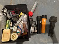 Black carrying bag with assorted flashlights, bulbs, batteries, and small hand tools packed inside.