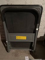 Folded view of gray flat dolly showing foldable U-shaped handle with black grips, ribbed platform surface, and metal frame.