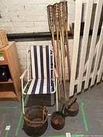 Photo of 4 lawn chairs with metal white frames and blue/white striped fabric next to 4 bamboo outdoor torches, an antique wooden pail, iron kettle, and iron pot.