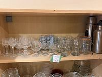 Shelf containing clear glassware including brandy glasses, wine glasses, beer flutes, and glass jars with orange seals.