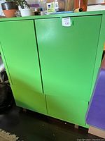 Front view of green wooden cabinet with closed doors and drawers, showing minor scuffs and flat green finish.