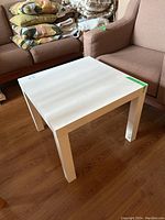 Photo of white IKEA Lack side table showing table top and legs in living room setting with visible scratches.