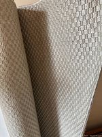 Close-up of flatwoven basket-weave textured pattern of a beige rug, showing surface detail.