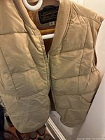 Close-up of beige quilted vest with ribbed collar, hanging on hanger, showing Eddie Bauer label and size 6 tag.