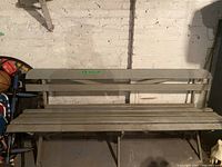 Picnic bench with wooden slats and backrest against brick wall in basement.