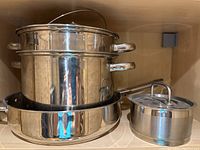 Shelved stainless steel cookware including steamer pot and smaller pot with lid.