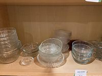 Photo of multiple clear glass bowls on a wooden shelf, showing small to medium round bowls and a textured bowl in the center.