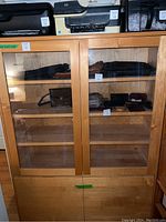 Front view of wooden shelving cabinet showing two upper glass doors with shelves inside and two bottom wooden drawers closed.