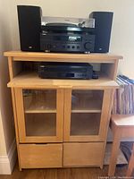Full view of the wooden stereo cabinet with audio equipment on top and records beside it.