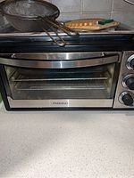 Closed front view of Paderno toaster oven on counter with mesh strainer and wooden board on top