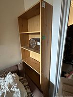 Photo showing the front and side angle of the tall wood bookshelf with three shelves and an item on one of the shelves.