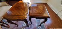 Photo showing two antique nesting tables with wood grain tops and carved legs, placed on a floral area rug.
