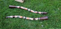 Both didgeridoos laid on grass showing full length and painted designs.