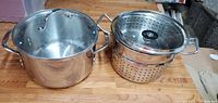 Photo showing the two stainless steel pots side by side; the smaller pot contains the perforated steamer strainer insert.