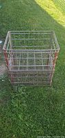 Two stacked vintage heavy metal milk crates on grass, showing rectangular wire grid design with rust and wear.