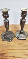 Pair of silverplate candlesticks standing side by side on wooden surface, showing hexagonal bases and tapered column design
