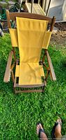 Front view of the antique fold-up chair showing yellow fabric seating and teak-like wood frame