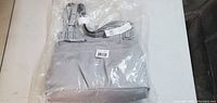 Gray handbag new in original plastic packaging showing front and top handles with tags visible.