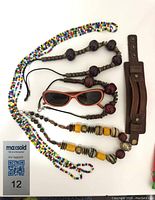 All items in lot arranged flat on white surface including two long beaded necklaces, three shorter leather cord beaded necklaces, sunglasses, and leather cuff bracelet.