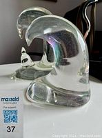 Two clear blown glass sculptures with smooth shapes, one larger and one smaller, shown side by side.