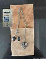 Photo showing the silver earrings with black onyx stones and filigree heart locket necklace laid on a suede pouch.