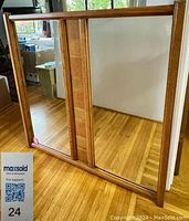 Overall view of the oak framed mirror showing the two-panel mirror design and oak frame with visible wood grain and scratches, on a wooden floor background.