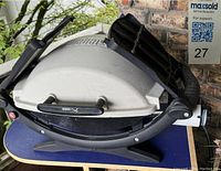 Weber Mini barbeque grill showing white lid with logo, black frame and foldable side shelves.