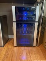 Front view of dual compartment wine fridge on wood floor with blue LED lighting visible
