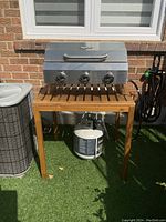 Frontal view of stainless steel NXR grill head mounted on wooden stand with propane tank below