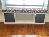 Front view of white wooden storage bench with floral cushion on top and two gray fabric bins in side cubbies.