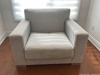 Front view of a single upholstered armchair with light gray fabric and wooden block feet on a hardwood floor.