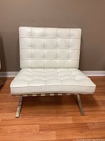 Front view of white leather tufted chair showing seat and backrest with button details and stainless steel base.