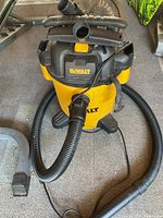 Front view of Dewalt shop vacuum with flexible hose attached, resting on carpeted surface near weight plates.