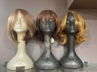 Front view of three synthetic wigs on three styrofoam wig stands, showing different styles and colors.
