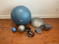 Wide view of all fitness equipment together on wooden floor including balls, balance trainer, push-up handles, and pads