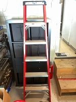 Full view of red fiberglass step ladder with 5 steps standing upright.