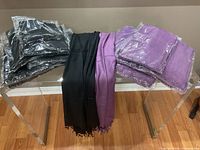 Lot showing black scarves in plastic packaging on left, black scarf loose in the middle, and purple scarves, some loose and some packaged on right.