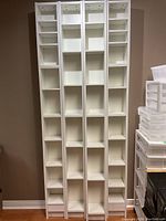 Front view of four tall white shelving units against a brown wall