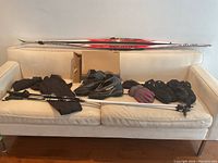 Cross-country skis, poles, boots, gloves, and apparel arranged on cream sofa showing lot contents