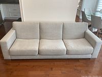 Front view of the light beige three-seater upholstered sofa with clean lines and removable cushions, placed on wooden flooring.