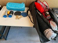 Full view of lot showing playing equipment on a table and inside a carrying bag, including rackets, net, and table tennis items.