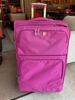 Front view of a pink soft-sided rolling suitcase with telescopic handle extended and two zippered pockets on the front