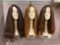 Three wigs displayed on foam mannequin heads: two brown and one blonde.