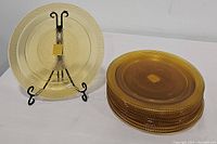 Stack of 9 amber glass round chargers with 1 displayed on a black metal stand showing textured pattern and amber color.