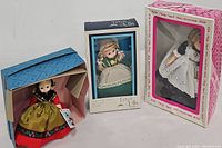 Three vintage dolls in their original packaging, front view showing the 1992 Shirley Temple Doll in pink and white box, 1979 Playmates Ireland Tiara Doll in cream and blue box, and Madame Alexander Sweden doll partially out of blue box.