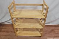 Front view of the natural wood 3-shelf foldable bookshelf showing the three flat shelves and side slats.
