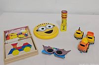 Full view of lot showing Melissa & Doug blocks and boards, Curious George kaleidoscope, three toy cars, and kids sunglasses