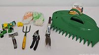 Overview of garden tools including hand rake, pruning shears, garden fork, gloves, hose connectors and spray nozzle in a line on flat surface