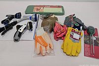 Photo showing assortment of garden gloves, three hose nozzles in packaging, and a green padded kneeling pad with floral design.