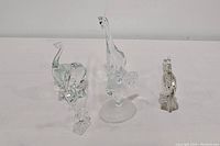 Five vintage solid clear glass animal figurines on a white surface: giraffe, rooster, fish, elephant, and horse.